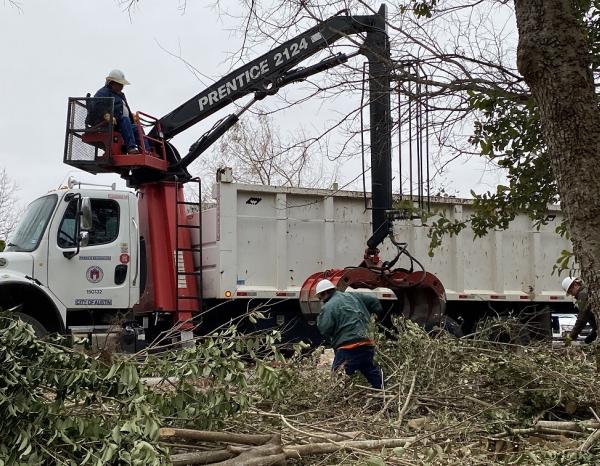 A man operating heavy machinery while picking up downed branches from a tree.