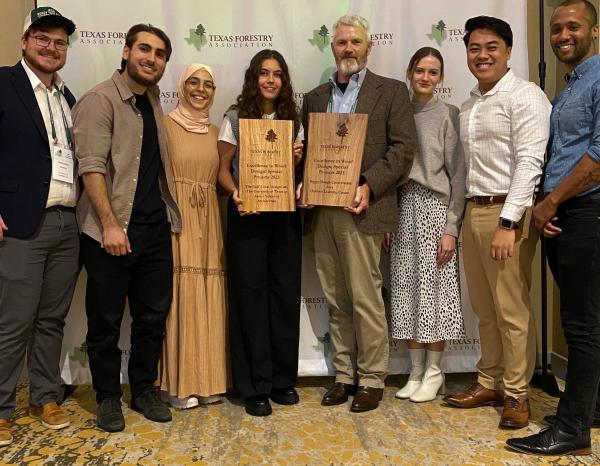 Students smiling at the camera as they hold up their Excellence in Wood Design Award from the Texas Forestry Association