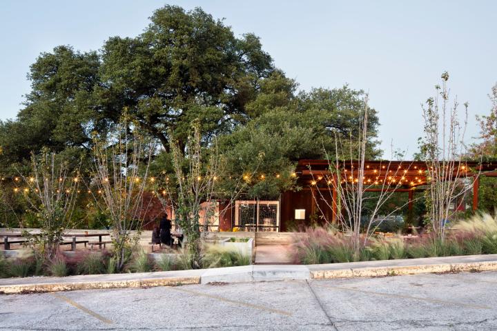 Exterior shot of Texas French Bread seen from the parking lot, with lights hanging over the patio and a large shade tree out in front of the building