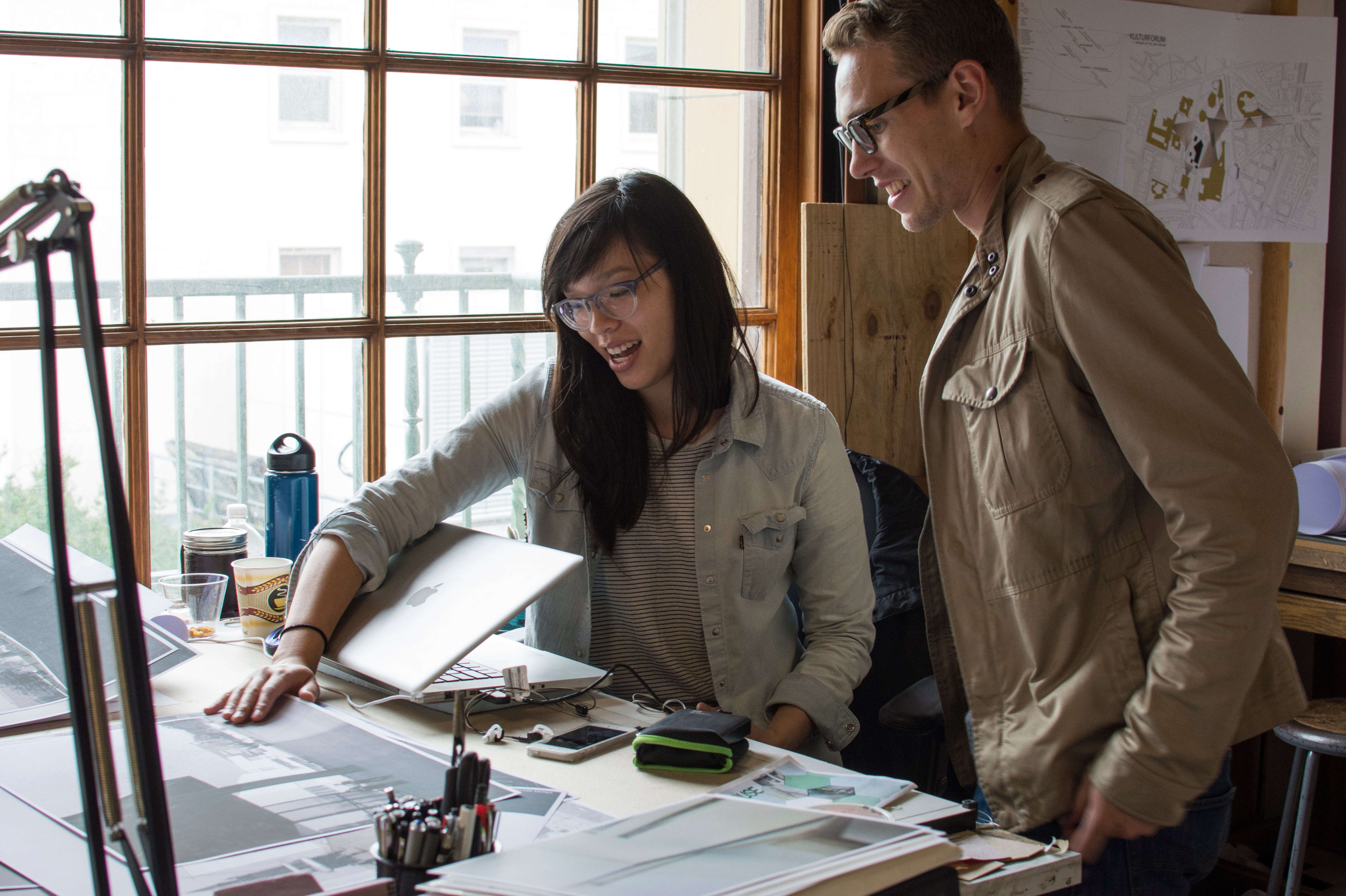 Two students in glasses smile while looking over materials in studio