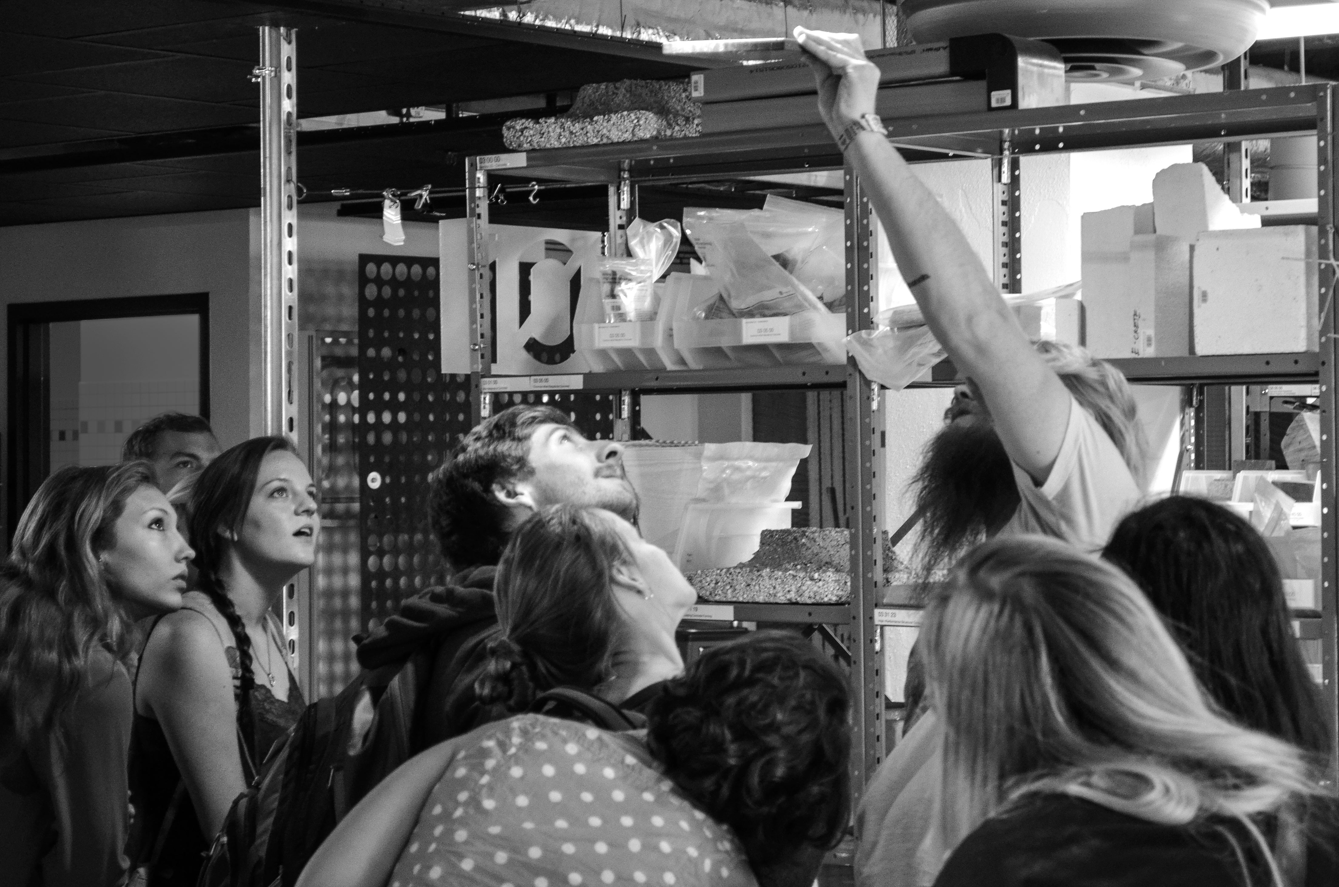 Black and white photo of students looking up at a material sample that someone is holding up to an overhead light