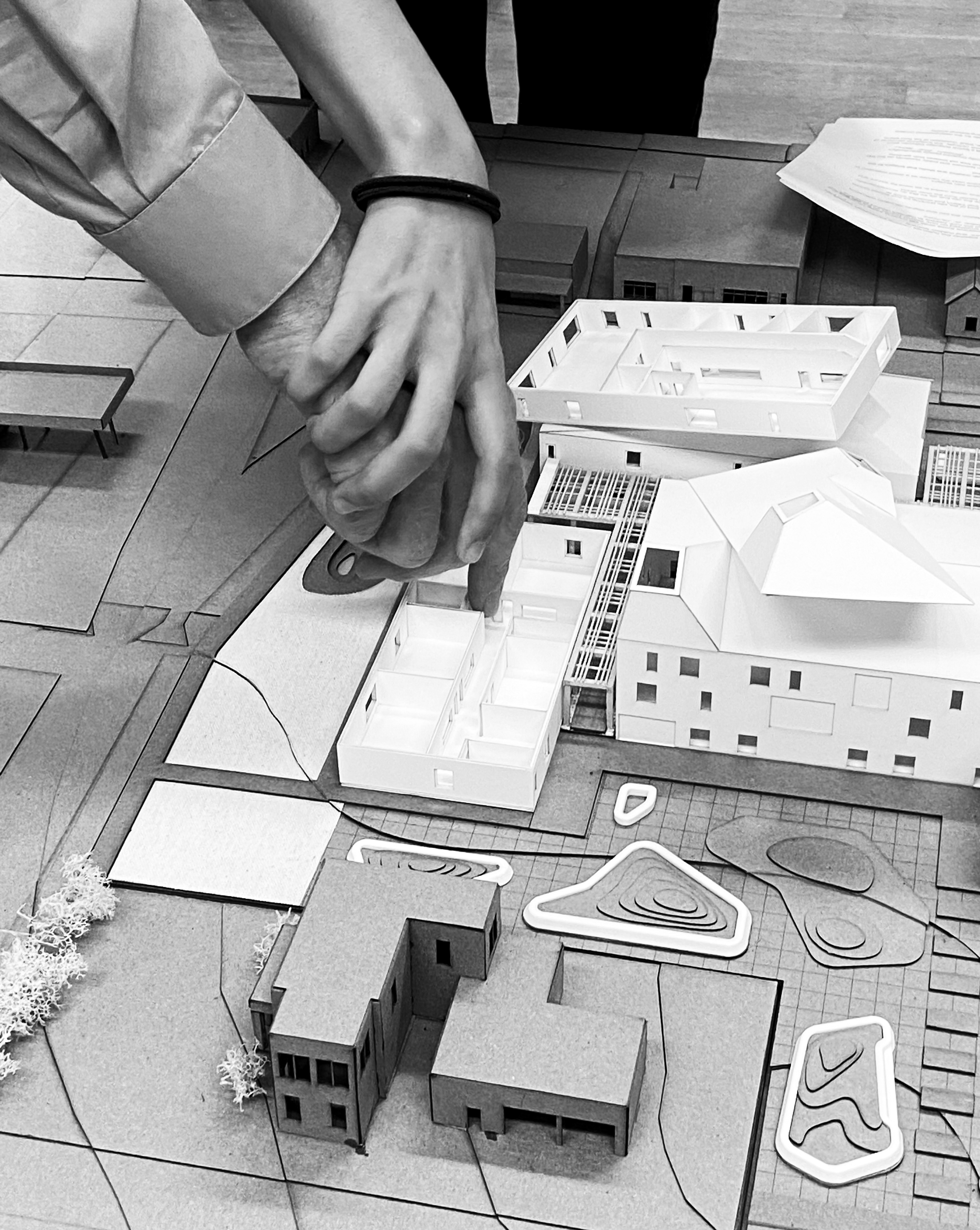 Black and white photo of a hand guiding another person's hand towards an architectural model
