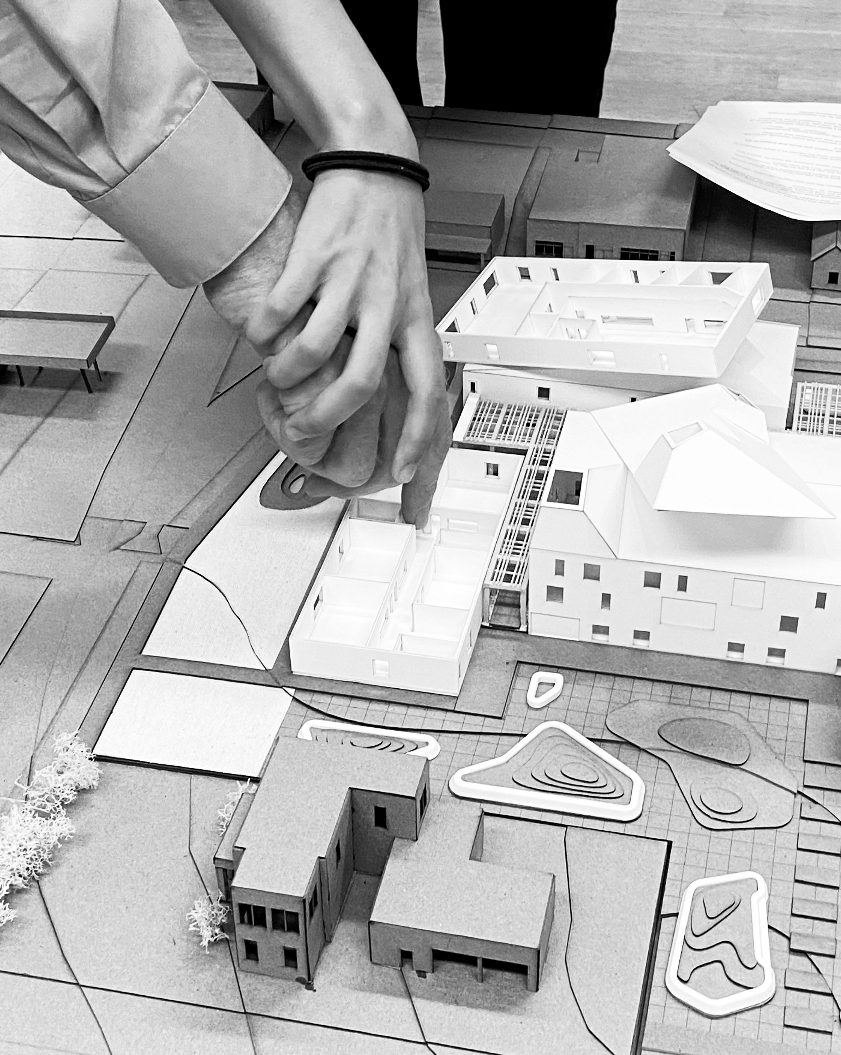 Black and white photo of a hand guiding another person's hand towards an architectural model