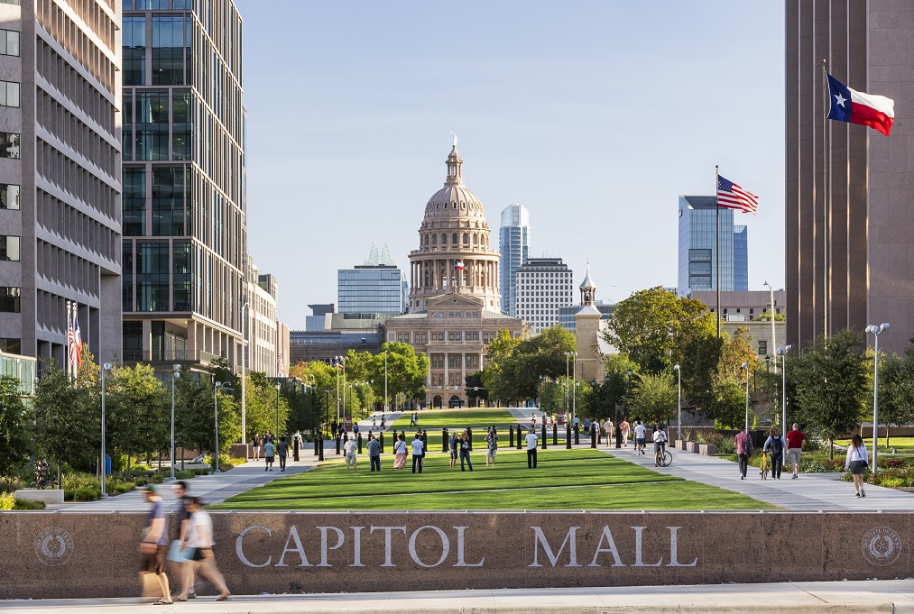 Street-level view of the Texas State Capitol looking across the Capitol Mall where people gather.