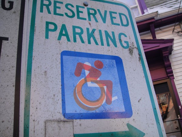 Wheelchair "Reserved Parking" sign with a drawing of a person racing in a wheelchair over the typical one