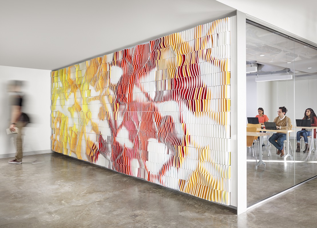 Students sitting in a high-tech classroom behind a digitally manufactured wall comprised of thousands of colorful tiles