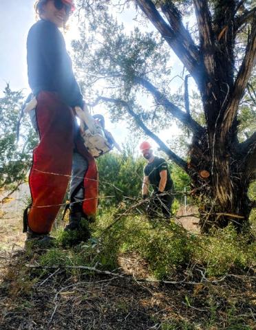 Two people smiling at the camera as they take a break from breaking down brush and tree limbs.