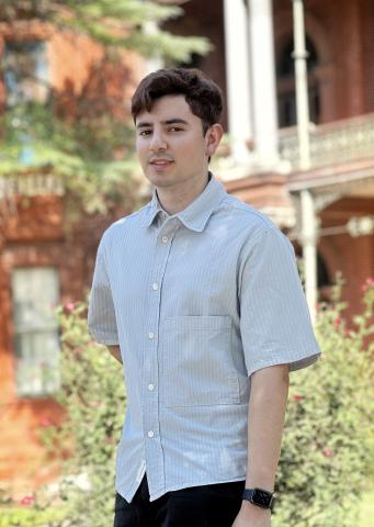 David stands in front of a building with foliage, smiling at the camera