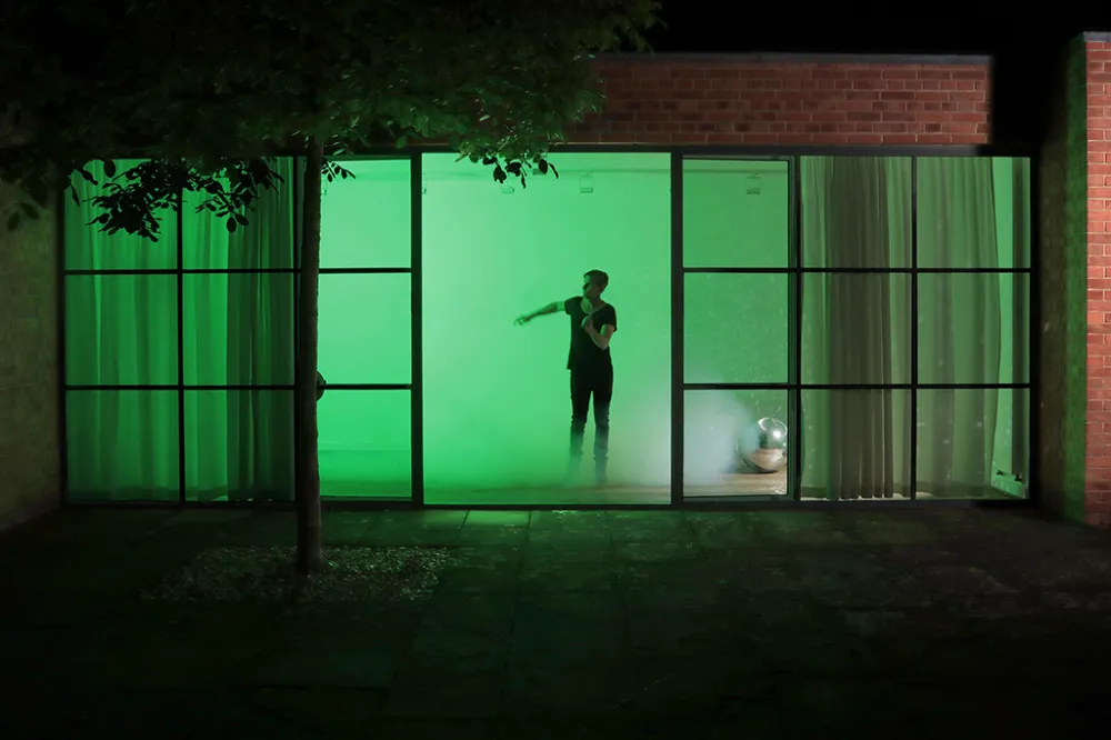 A silhouette seen through open floor-to-ceiling windows dancing in what looks like a cloudy green room