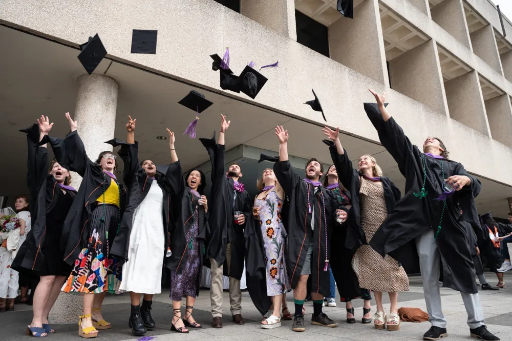 Students celebrating at commencement as they throw their caps into the air simultaneously.
