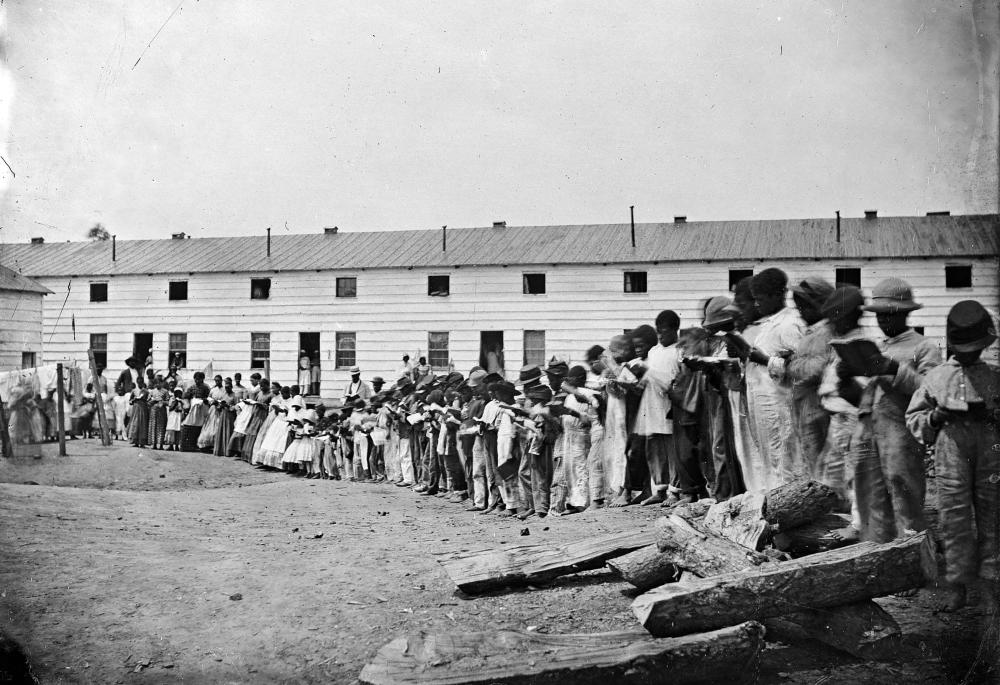 Black and white historical photo of group of African Americans standing in front of a building