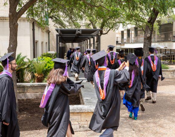 Students in regalia walk across the West Mall to the School of Architecture's commencement ceremony