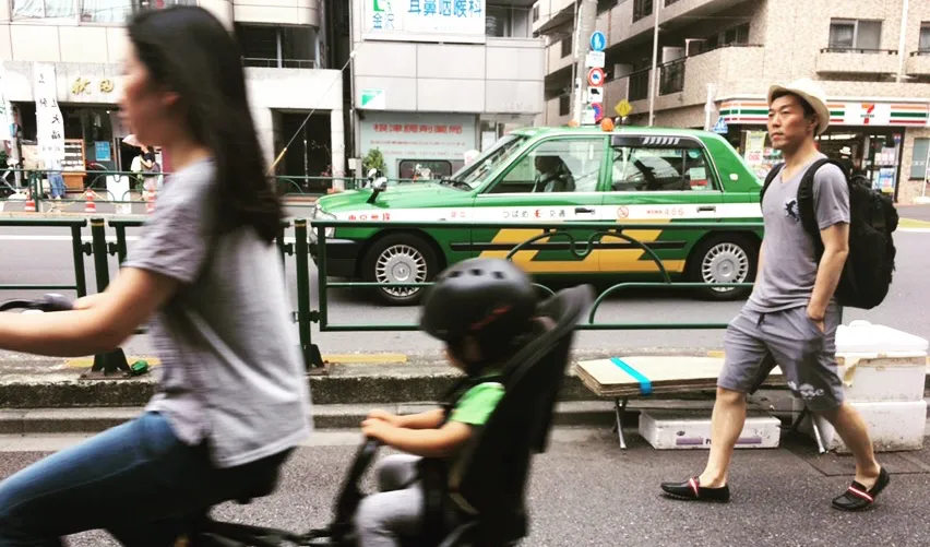 Woman riding bike with baby in Tokyo as man walks by