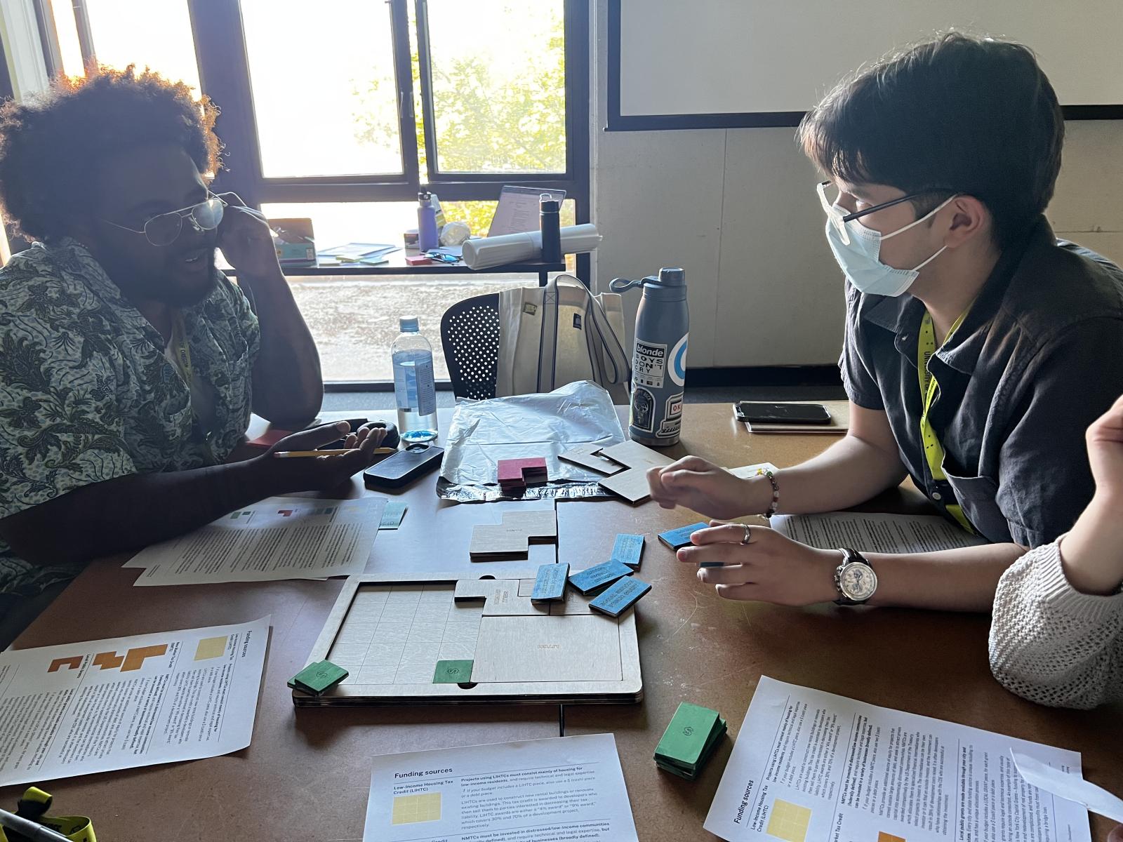 Students in discussion around a table strewn with papers and blocks