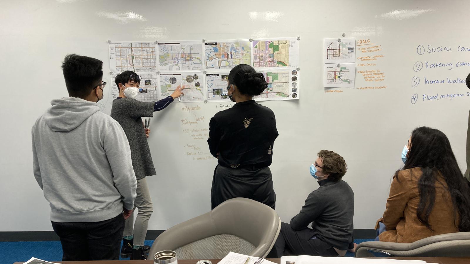 Tatum Lau pointing to diagrams and drawings on a wall while others look on and listen