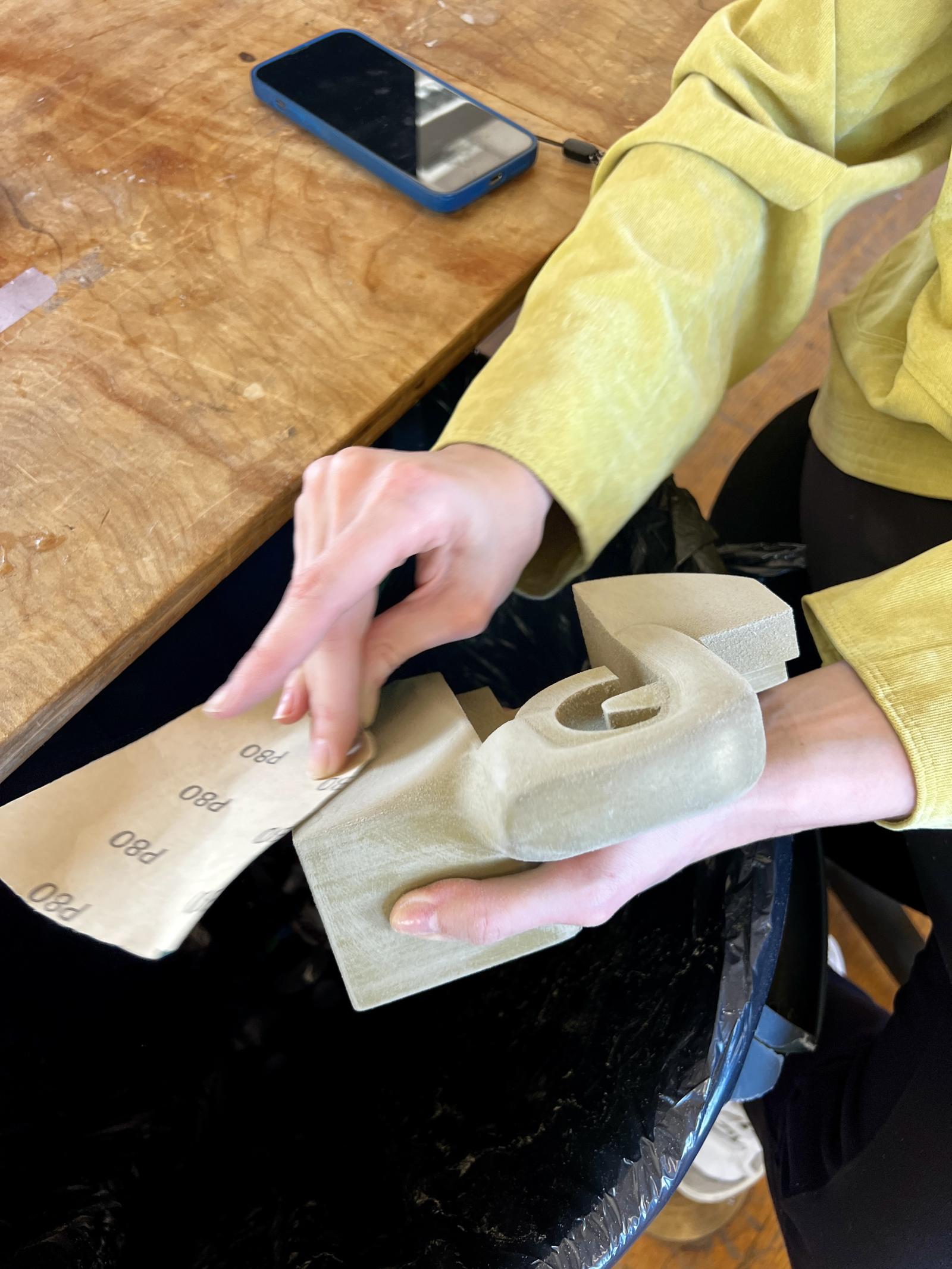 A close up of a student's hands as she sands her model