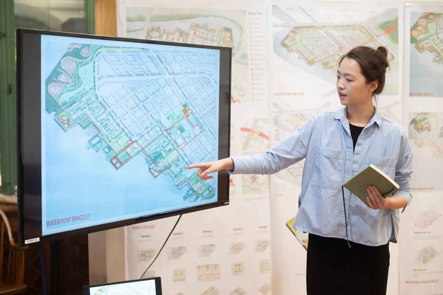 A student points at a television screen as she gives a final review presentation in front of her pinned up work