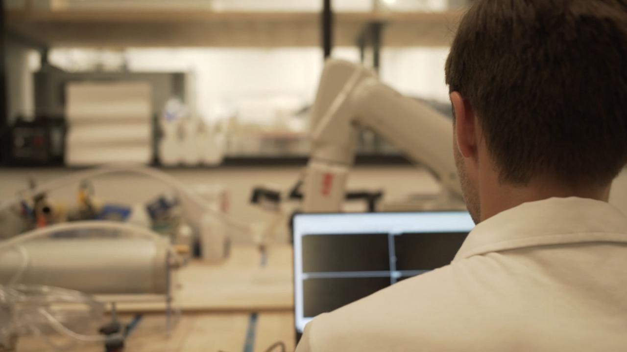 View of Patrick Danahy from behind looking over his shoulder at a computer and white machinery in the background