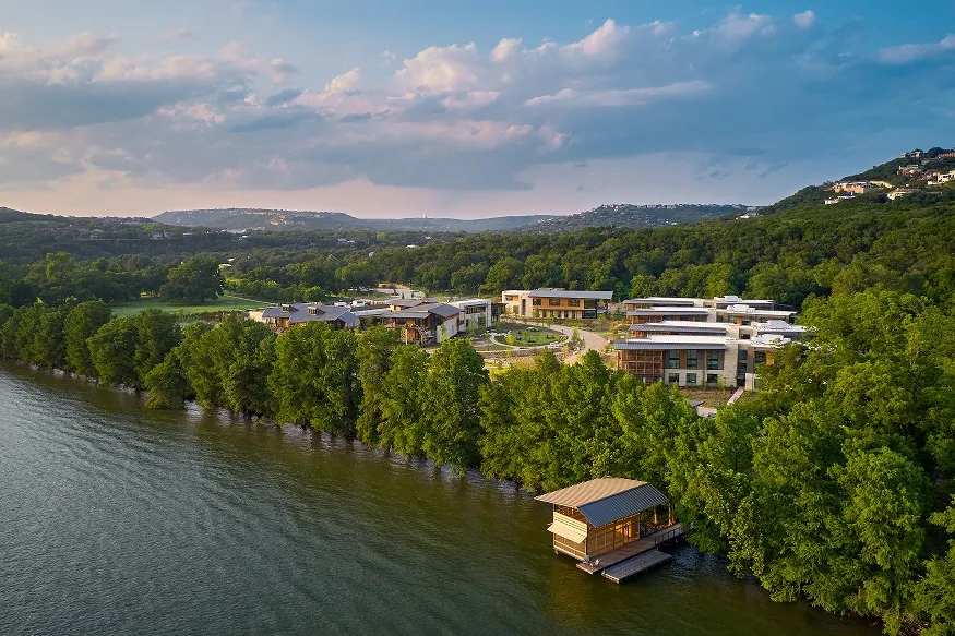 Aerial shot of the Holdsworth Center on the edge of Lady Bird Lake with green space and a sunset behind it.
