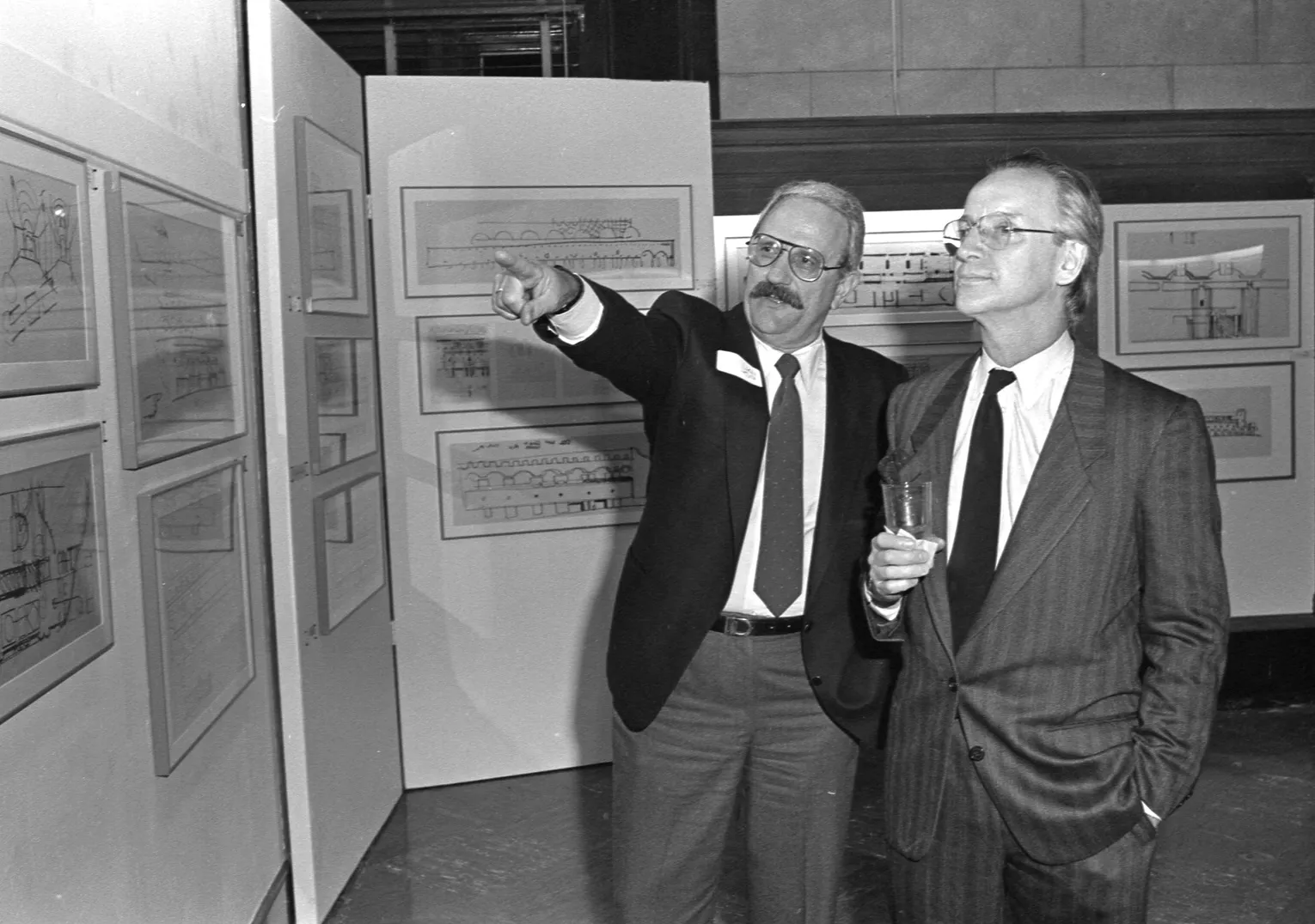 Two men looking at framed material, one of them pointing.