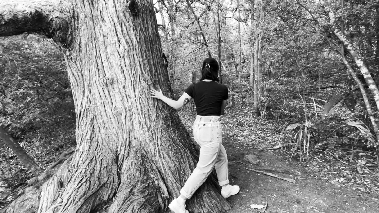 girl walking past a large tree on a forest path