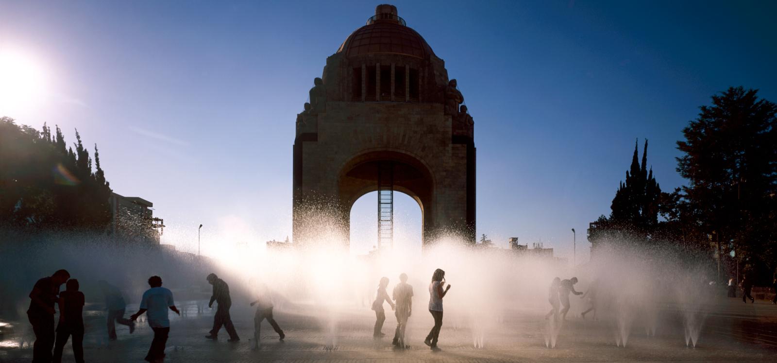 Exterior of arched building and concrete park with water fountains