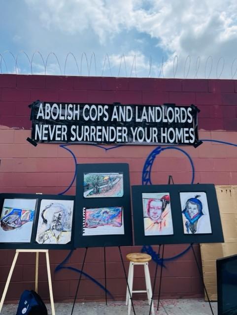 Artwork outside of a building with the sign "Abolish cops and landlords, never surrender your homes."