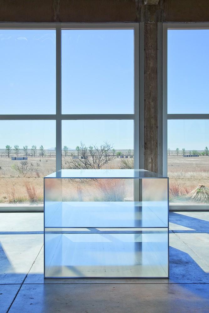 Image of a structure in front of floor to ceiling windows. The structure is reflective or transparent in a way that creates an interesting perspective or illusion.