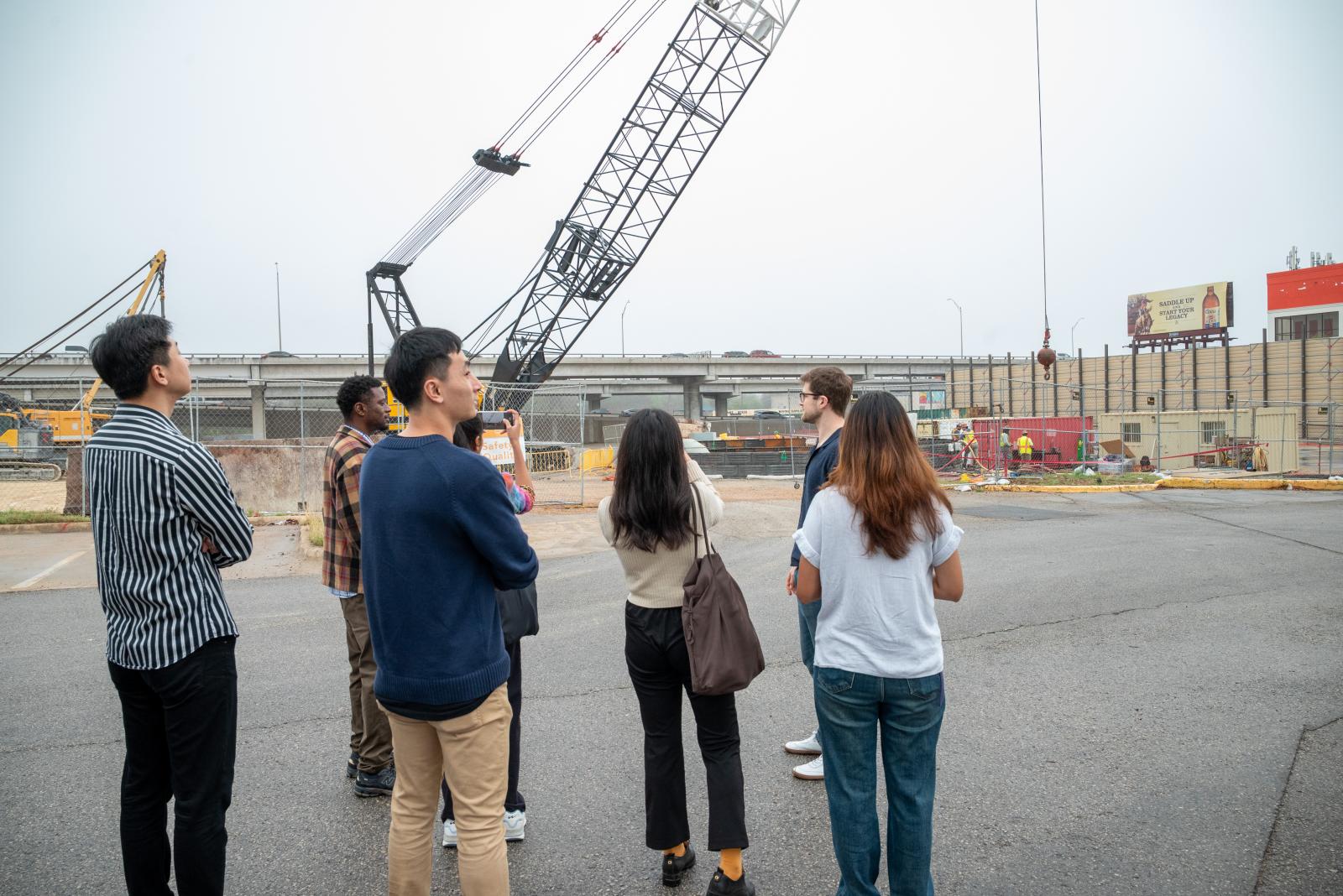 students look at a construction crane, taking photos. Their backs are to the camera.