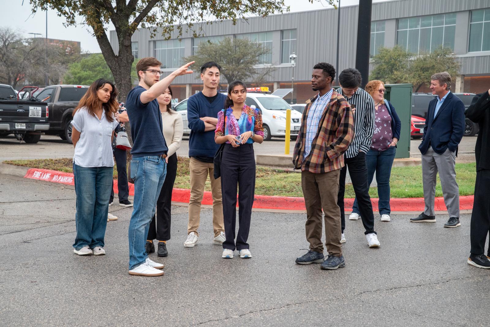 A group of students gathered in a parking lot, looking out into the distance. 