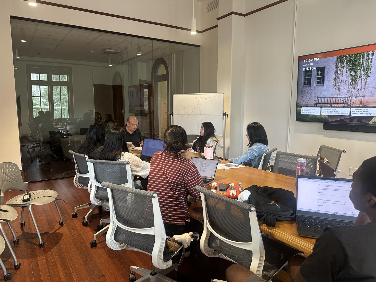 A man sits at a table teaching a group of six students