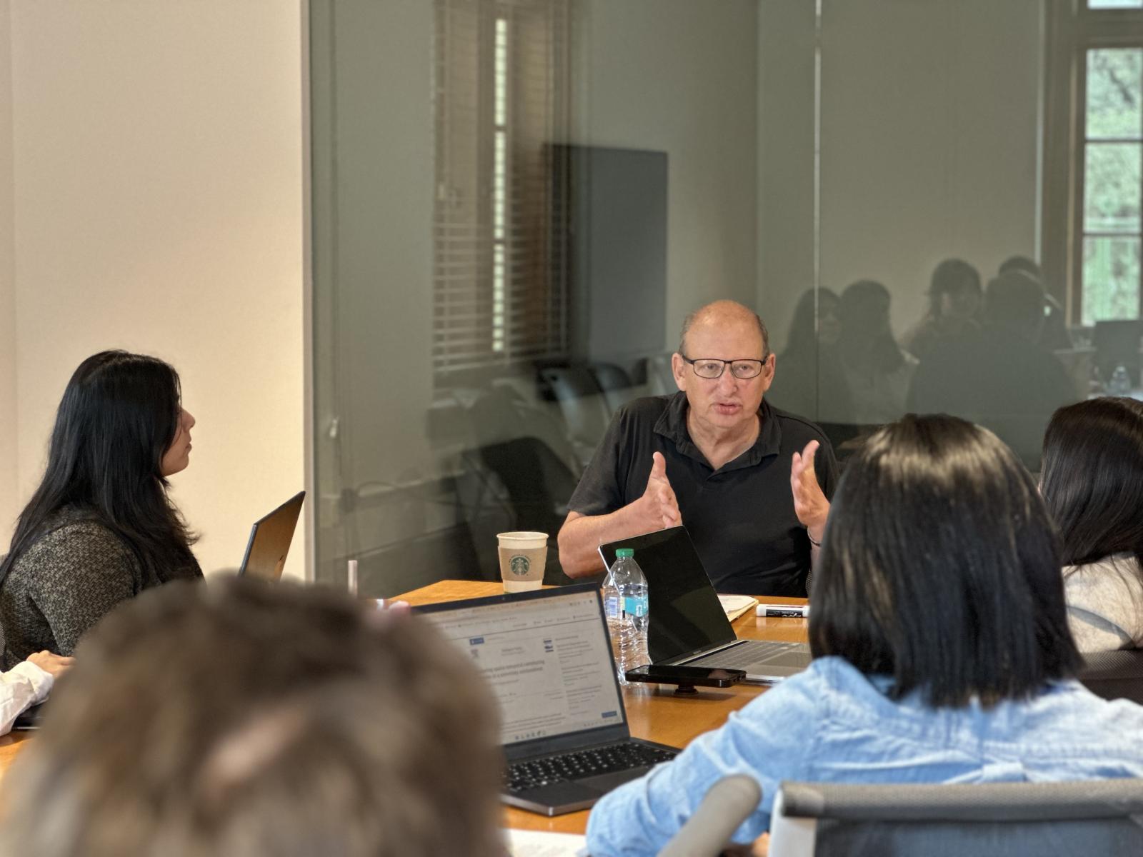A man sits at a table teaching a group of students