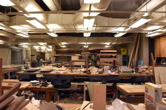 Student stands in a chaotic, messy wood shop