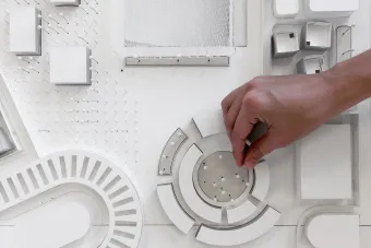 White architecture model seen from above with a students hand adjusting something