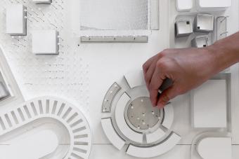 White architecture model seen from above with a students hand adjusting something