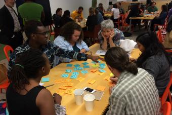 A diverse group gathers around a table with post-it notes