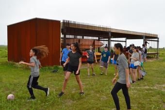 A group of children play soccer in a field in front of a Gulf Coast DesignLab structure