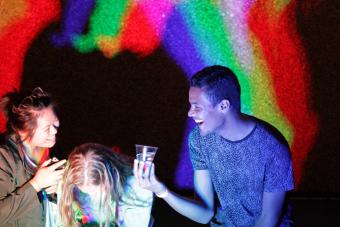 Three students laughing in front of a rainbow colored background