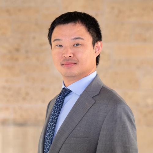 Associate Professor Junfeng Jiao is photographed wearing a suit and tie in front of a plain background. 