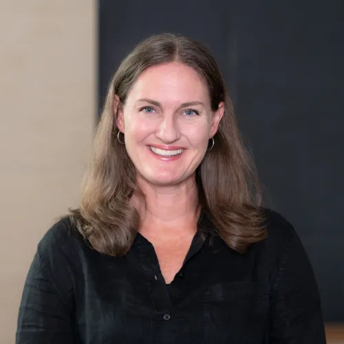 	This is a headshot of Katherine Lieberknecht from the shoulder up. Katherine is standing in front of a blackboard and smiling at the camera