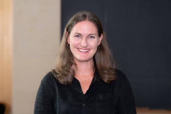 	This is a headshot of Katherine Lieberknecht from the shoulder up. Katherine is standing in front of a blackboard and smiling at the camera