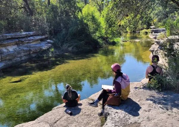 Landscape architecture students drawing as they look out over a water feature in Austin, Texas