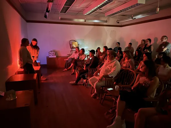 Interior design students gather in a dark red-lit room with Jorge Pardo to display their illuminated creations