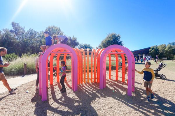 Several children climbing on and interacting with a vibrantly colored set of arches at the Wildflower Center's Fortlandia