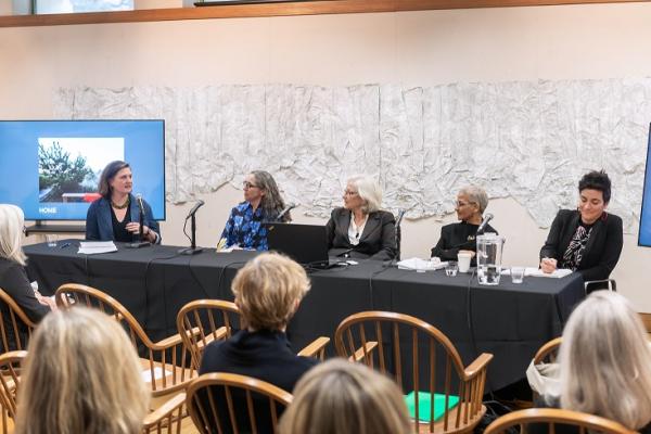 Several women sit on a panel in front of an audience