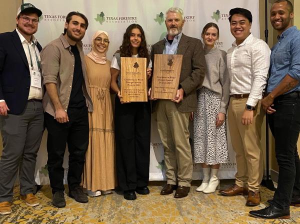 Students smiling at the camera as they hold up their Excellence in Wood Design Award from the Texas Forestry Association