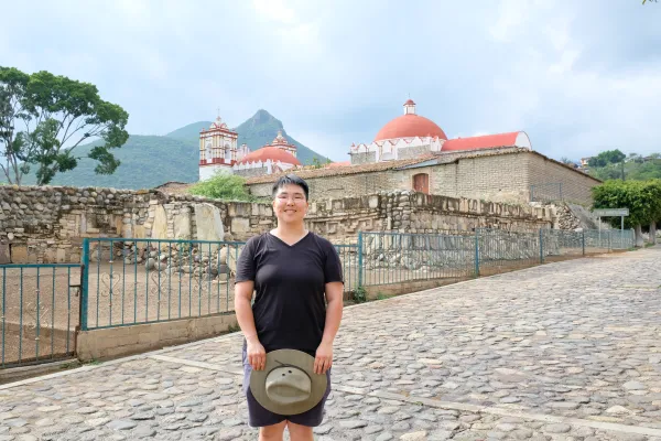 Ji Yoon stands in front of Teotitlan with their hat in their hands.