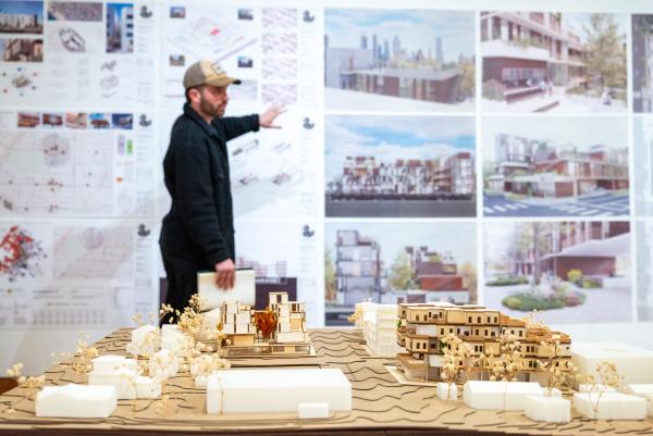 A student presenting work during final reviews with a large architecture model in the foreground.
