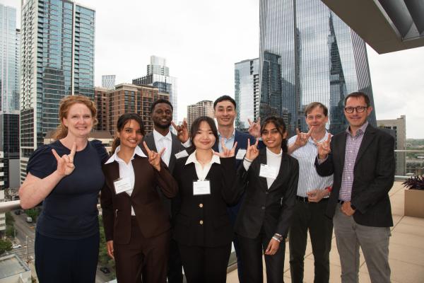 Five students pose with three faculty members, doing a hook em horns hand sign