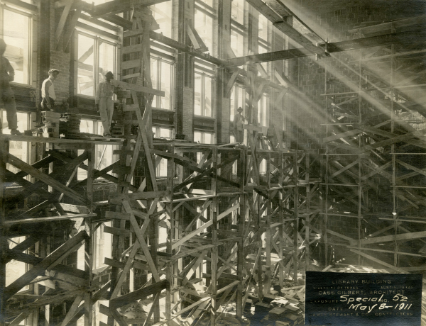 Historic photo of Battle Hall under construction in 1911 showing light pouring through floor-to-ceiling windows and men standing on wooden scaffolding inside